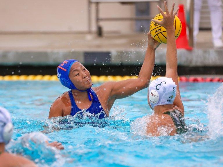 An action shot of water polo player Namlhun Jachung in the pool. Another player attempts to block as Jachung holds up the yellow ball.